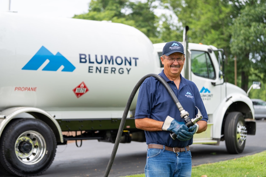 Happy Blumont Energy service technician looking at the camera while pulling a hose from a propane truck in the background