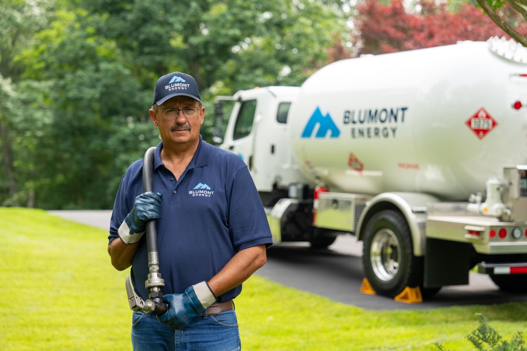 service technician looking at the camera while pulling a hose from a propane truck in the background