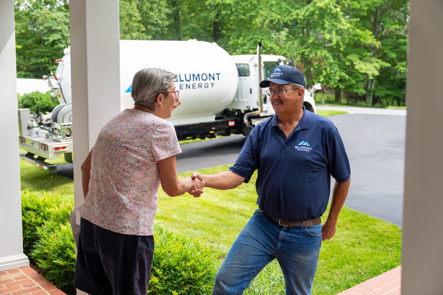 happy customer shaking hands with a Blumont Energy service technician with a propane truck in the background